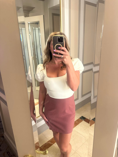 80s mom taking a mirror selfie in a white top and pink mini skirt